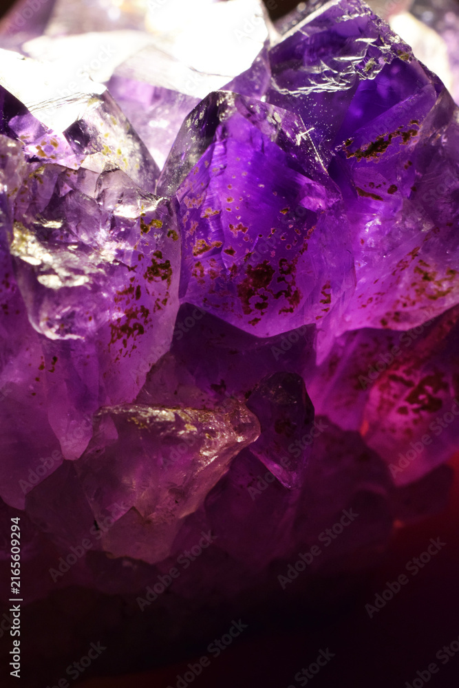 Fototapeta premium A close-up of a crystalline purple amethyst mineral stone. Selective focus. Macro photography of precious and semi-precious stones. The shiny surface of the precious crystal.
