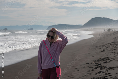 Canvastavla Woman in pink clothes stands on black volcanic beach with Pacific waves and distant mountains at Khalaktyrsky Beach, Kamchatka