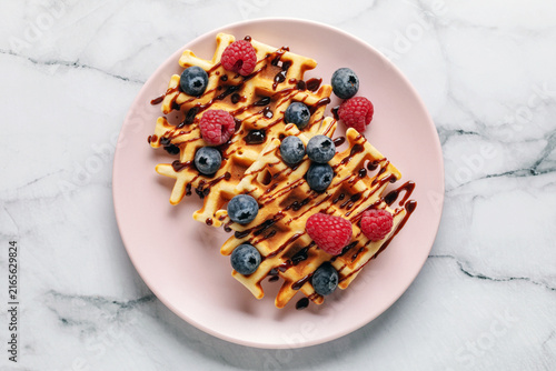 Homemade waffles with chocolate sauce and berries in plate on the table. Top view