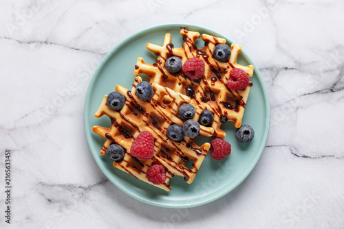 Homemade waffles with chocolate sauce and berries in blue plate on the table. Top view