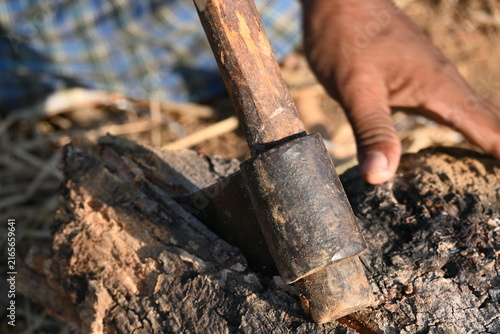 Fotografie A person using a traditional hand axe to hew a rough wooden log resting