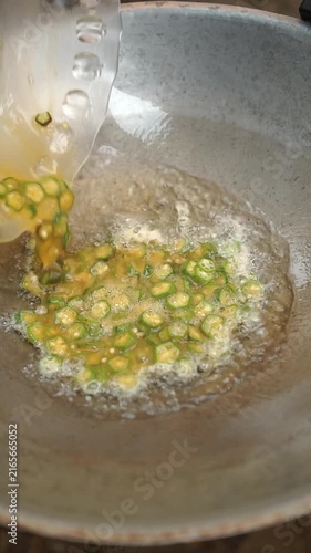Cooking Thai okra omelet (Kai Jeow Kra Jeab Khiew). Whisking eggs with seasonings, mixing with sliced fresh okra, and deep-frying in hot oil until golden brown and crispy.