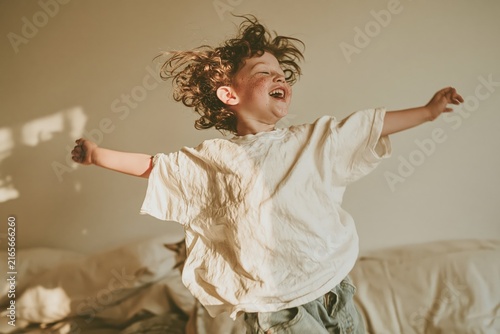 Happy child jumps on a bed with five pillows