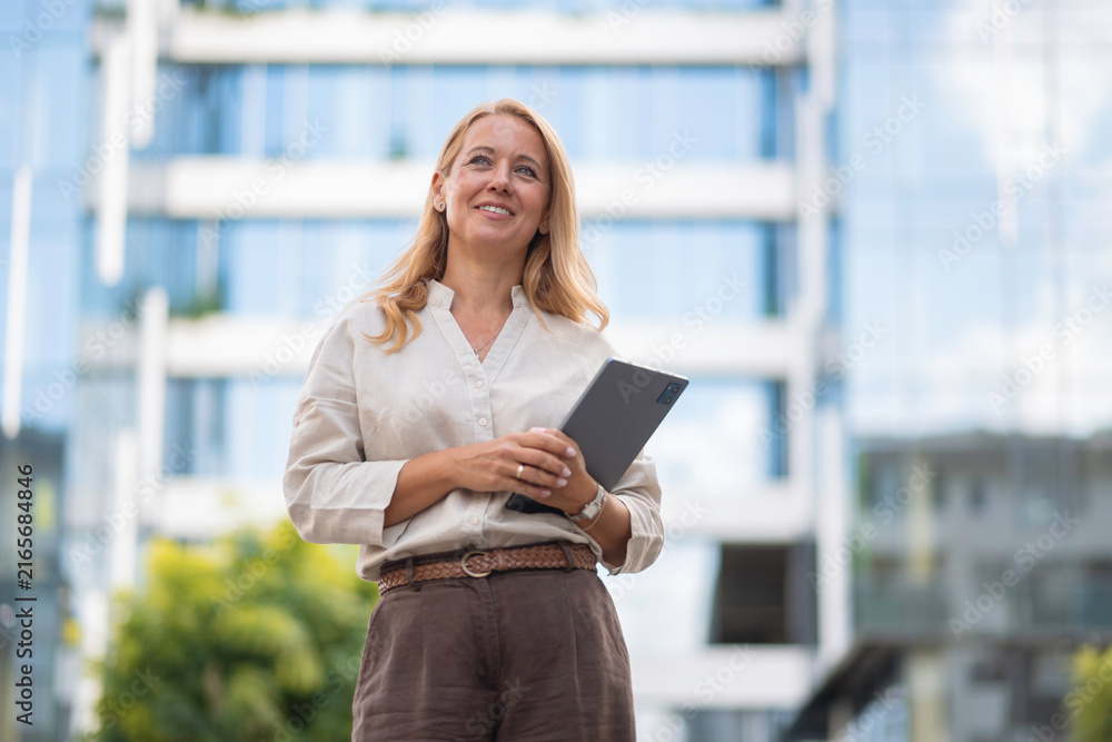Fototapeta premium Businesswoman smiling, holding a digital tablet in an urban setting