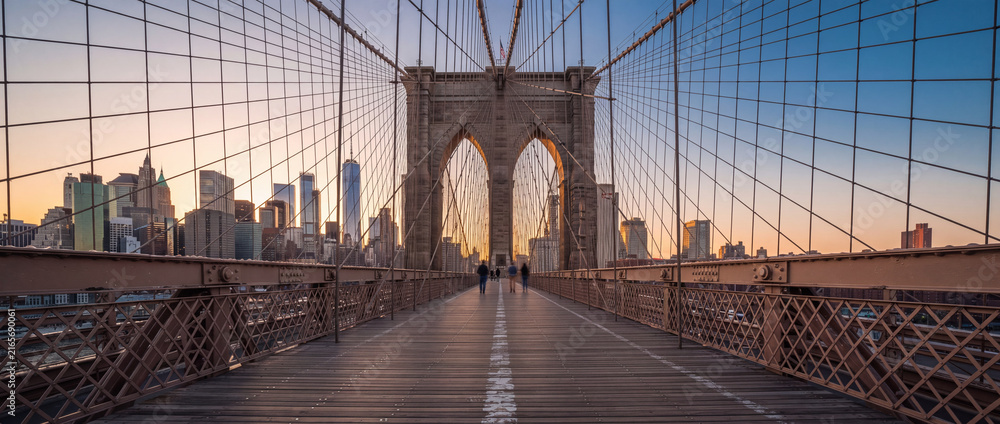 Fototapeta premium Brooklyn Bridge pedestrian walkway at sunrise with suspension cables framing the Lower Manhattan skyline in warm morning light, ideal for urban travel and tourism concepts