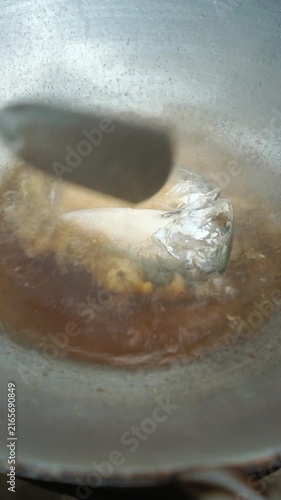 Cooking Thai fried short mackerel topped with garlic (Pla Too Po Kra Thiam). Deep-frying mackerel until crispy, frying crushed garlic until golden, and serving together on plate.