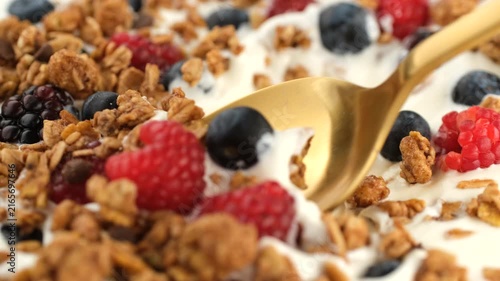 Greek yogurt with granola and fresh berries scoop with spoon, close up. Healthy protein, fiber breakfast or snack
