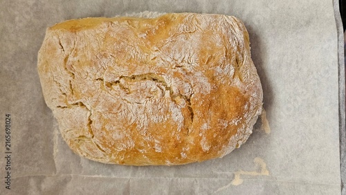 Foto A freshly baked rustic loaf of bread rests on parchment paper with a golden crusty surface dusted with flour