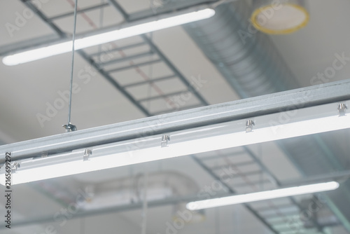Suspended modular LED lighting fixture with continuous trunking rail installed on a ceiling framework in a modern industrial warehouse