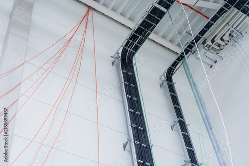 Suspended cable ladder racks routing structured power lines on a masonry wall symbolizing electrical engineering and industrial power distribution