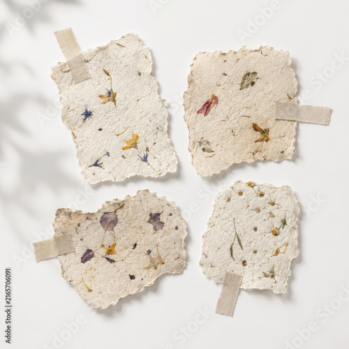 Four handmade botanical paper cards with dried flowers and tape on white background