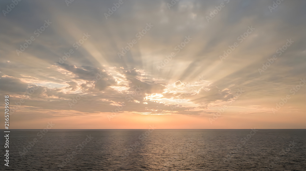 Fototapeta premium Dramatic ocean sunset with golden sun rays over calm sea horizon at dusk