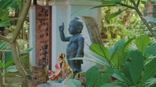 Buddha statue by tropical foliage in peaceful temple garden, Sacred Buddhist shrine framed by green leaves in tranquil Asian spiritual sanctuary 4k