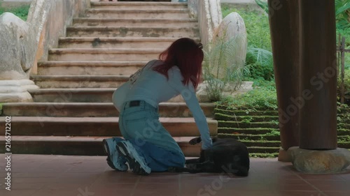 Woman petting resting stray dog beside temple staircase, Female traveler showing kindness to black dog at historic temple courtyard 4k
