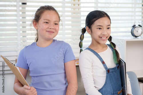 Foto Asian preteen girl holding notebook smiling beside caucasian classmate standing