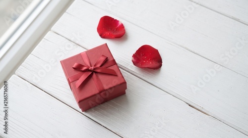 Red gift box with satin bow and heart-shaped chocolates on wooden table for Valentine's Day celebration