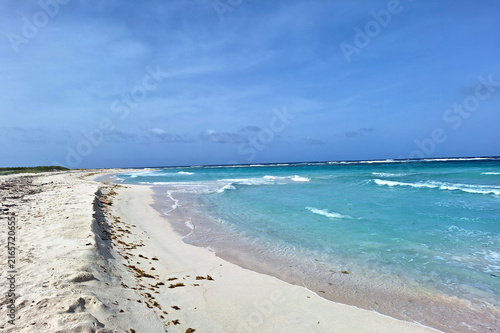 Scenic tropical beach with clear turquoise water, gentle waves, white sand, and a wide blue sky along an undeveloped coastline