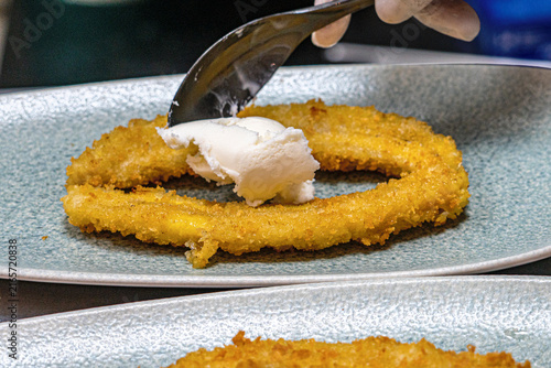  Professional chef hands plating a gourmet grilled banana dessert with vanilla ice cream and rich chocolate sauce.