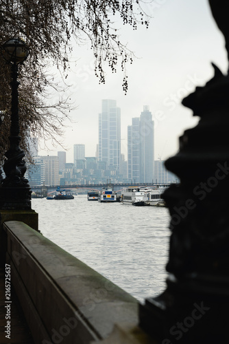 Photography Riverside promenade with boats and a view towards Vauxhall, London, framed by lamps, trees and a dark foreground structure