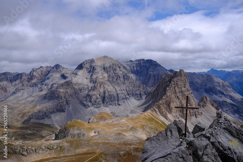 Konstfotografi Croix installée sur un sommet rocheux dominant un vaste panorama de haute montagne sous un ciel nuageux dans les Alpes françaises
