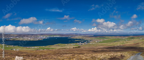 Wide coastal view of Lerwick Bressay and Viking Wind Farm in Shetland UK beneath dramatic blue skies