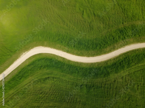 Aerial photograph of a winding dirt path cutting through vibrant green grass meadow fields