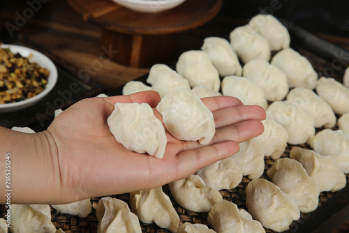 Foto Traditional Handmade Dumplings in Hand with Raw Dumplings on Bamboo Steamer - As