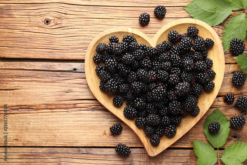 Naklejka premium Ripe blackberries with leaves on wooden table, flat lay. Space for text