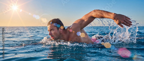 Man swimming in the open sea, doing crawl stroke with water splashes in sunlight, suitable for triathlon training, fitness campaigns, sports advertising, and outdoor summer recreation
