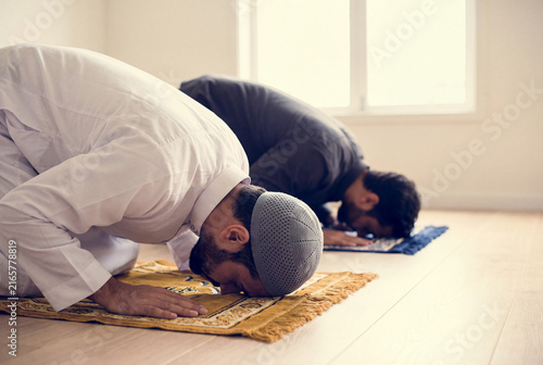 Muslim men in traditional white thobes prostrating on prayer rugs during worship of Islam at home
