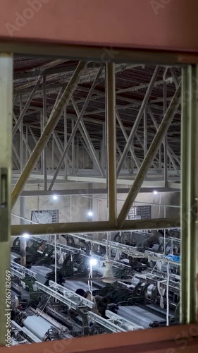 mechanical gears, thread bobbins, and rolled white fabric, with multiple weaving machines operating in the background.