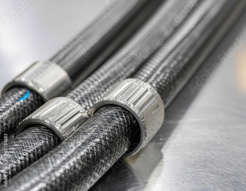 close-up of braided carbon fiber composite tubes and flexible industrial hoses with metal ring connectors in a modern technical manufacturing setting
