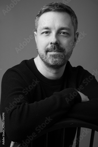 Foto Black and white studio portrait of a confident 44-year-old bearded man in a black sweater, photographed against a simple gray background