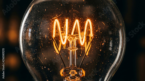 Incandescent light bulb filament glows warmly inside a glass enclosure close up photography
