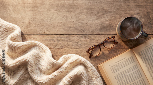 Flat lay of chunky knit blanket, glasses and book with steaming coffee