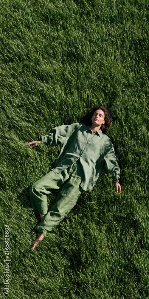 Fototapeta premium Top view of a woman lying on tall green grass in a matching outfit for lifestyle wellness background and banner design