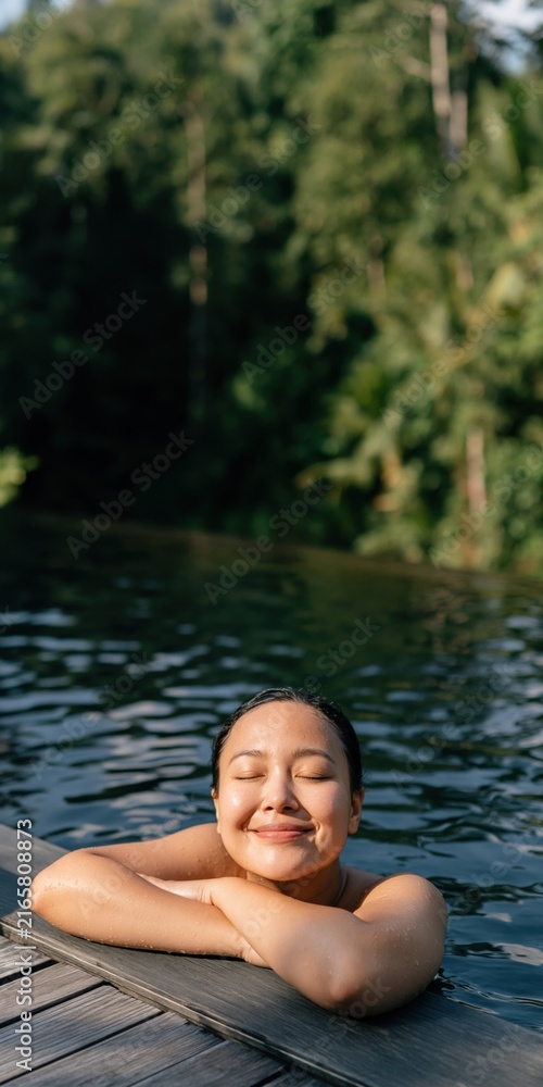 Fototapeta premium Woman smiling in pool at the edge with tropical trees in background for spa relaxation background and wellness poster design