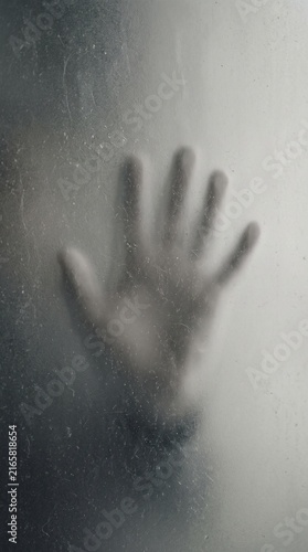Blurred human hand shadow silhouette pressed against frosted glass dark gray