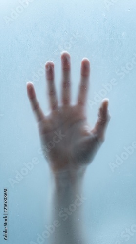 Human hand pressing against frosted blue glass surface from behind close-up