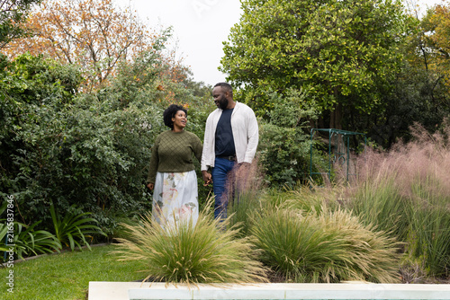 African couple walking holding hands beside pool edge in backyard, woman in floral skirt
