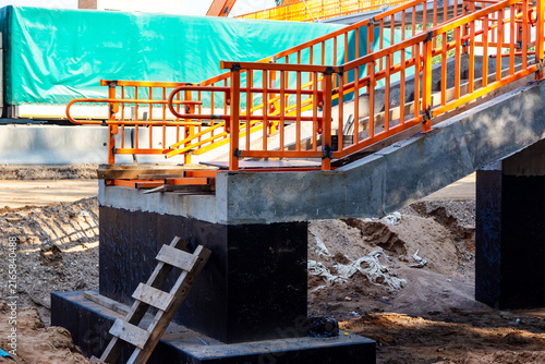 Foto Bright orange metal railings outline a concrete pedestrian bridge under construc