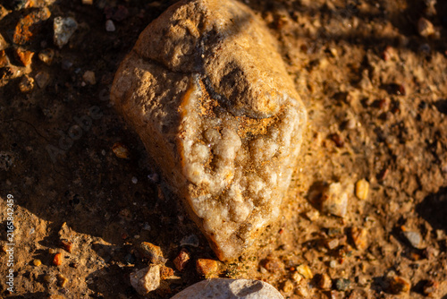 Фотография Close-up of a weathered quartz druse pebble lying on sun-drenched dusty ground,