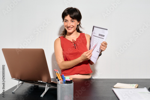 Woman Showing a CV during a job video call. She smiles confidently while holding papers near a laptop. 