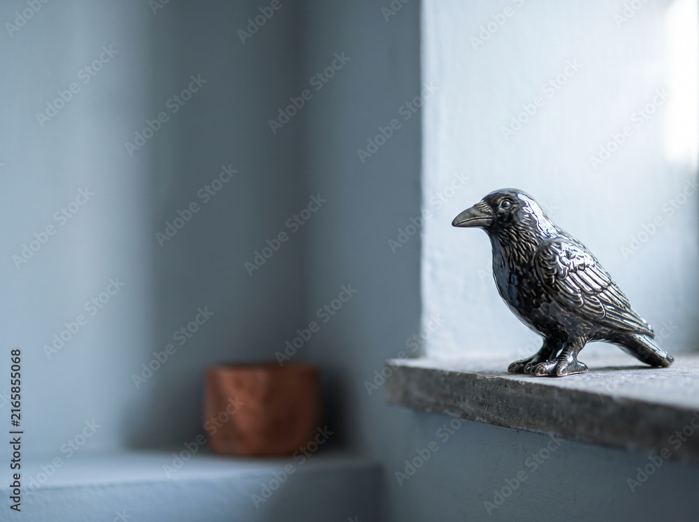 Naklejka premium A decorative black raven ceramic figurine standing on a stone windowsill inside a minimalist modern room illuminated by natural window light