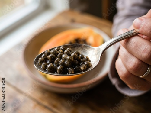 Person holding silver spoon filled with fresh tropical fruit seeds