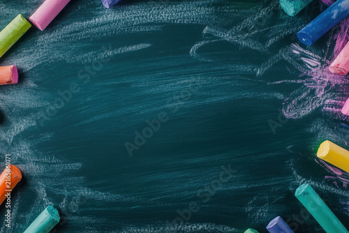 Colorful chalk pieces arranged around the border of a dark chalkboard background with copy space.