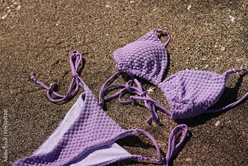 Canvastavla Lilac bikini swimsuit lies on a sandy beach, close-up