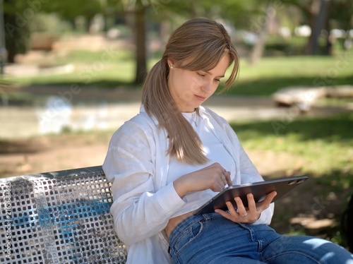 Bild auf Leinwand Young student scrolls through a tablet held on her lap while sitting on a metal