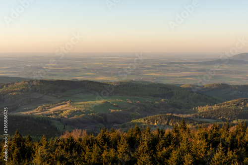 Cuadro en lienzo Expansive panoramic view of rural valley with green farmland, forests and distant settlements seen from high mountain viewpoint in soft golden hour light