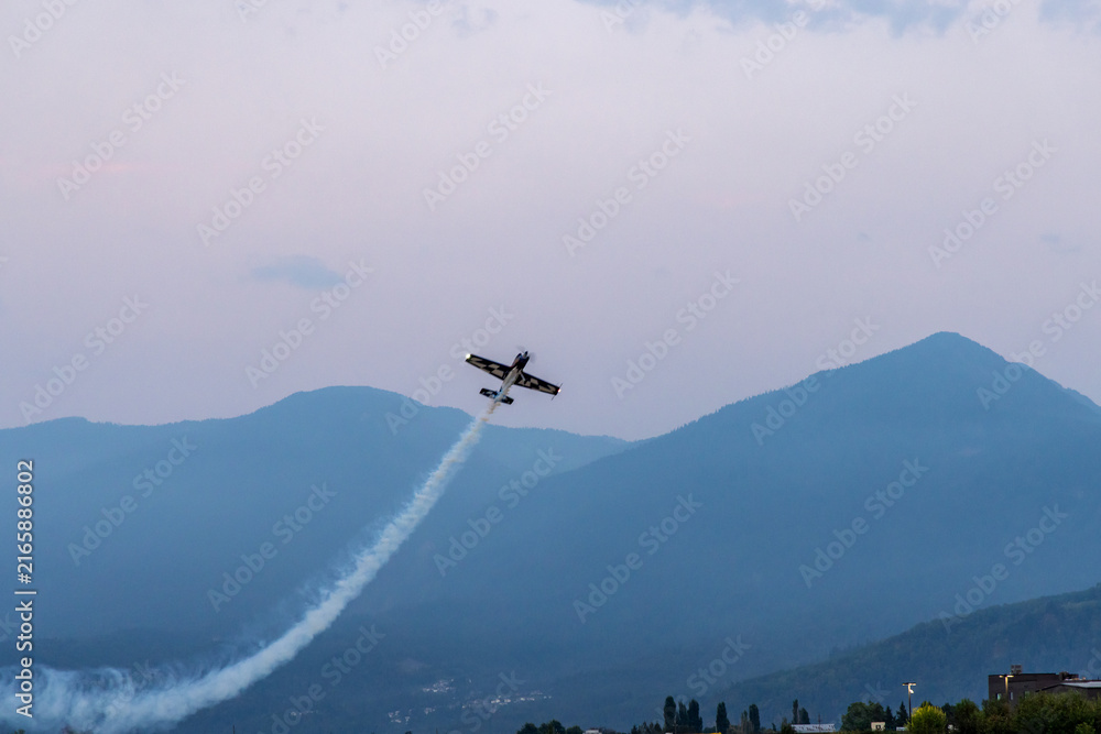 Fototapeta premium Aerobatic Plane Performing Smoke Trail Over Mountains At Air Show In Chilliwack, BC, Canada
